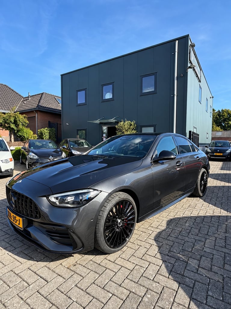 Grey Mercedes-AMG sports car on a brick driveway in front of a modern black house